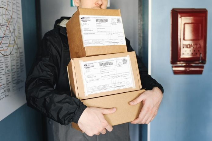 Muška osoba drži tri paketa u rukama ispred otvorenih vrata